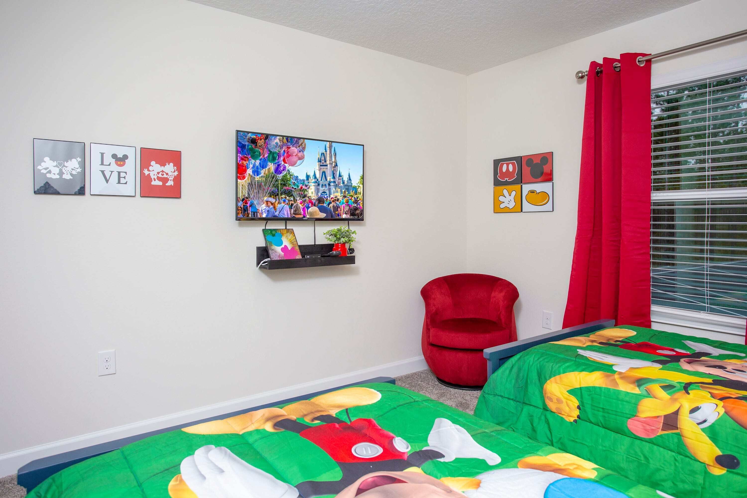 Quarto com duas camas, uma cadeira vermelha e arte nas paredes com Mickey Mouse e Disneyland.