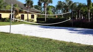 A volleyball court with a net, surrounded by a sandy area and greenery, with a building in the background. - Paradise 4Bd w Private Pool Waterpark 8951 (Kissimmee)