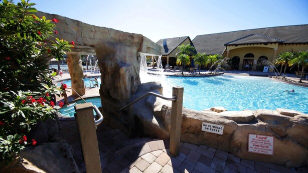 A pool area with a waterfall feature, a no climbing on rocks sign, and a poolside lounge area. - Paradise 4Bd w Private Pool Waterpark 8951 (Kissimmee)