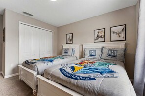 Quarto com duas camas, um guarda-roupa branco e três quadros na parede.