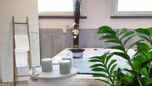Egy wellness-részleg, amelyben masszázságy, gyertyák, törölközőtartó és egy virágos növény található.