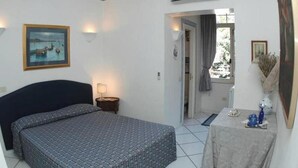 A hotel room with a bed, a small table with a vase, and a painting on the wall. - BLUE DREAM (Napoli)