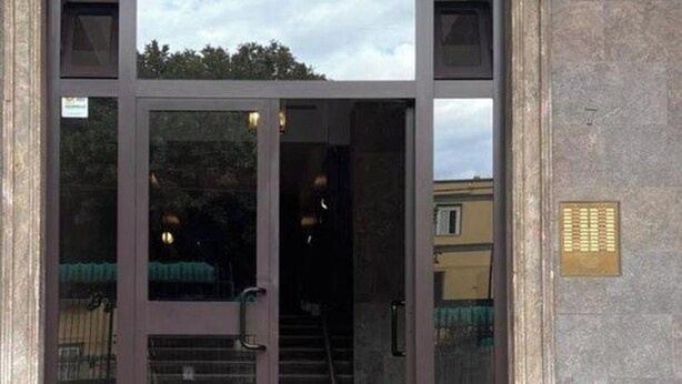 A building entrance with a large glass door, a metal gate, and a staircase leading inside. - BLUE DREAM (Napoli)