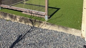 En inhägnad trädgård med konstgräs, ett trästaket och ett förråd.