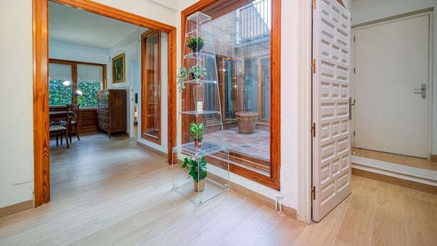 A hallway with wooden flooring, a glass door leading to a balcony, and a clear shelving unit with plants. - P Casa Cafe Madrid Calle Carlos Dubois 3 (Madrid)