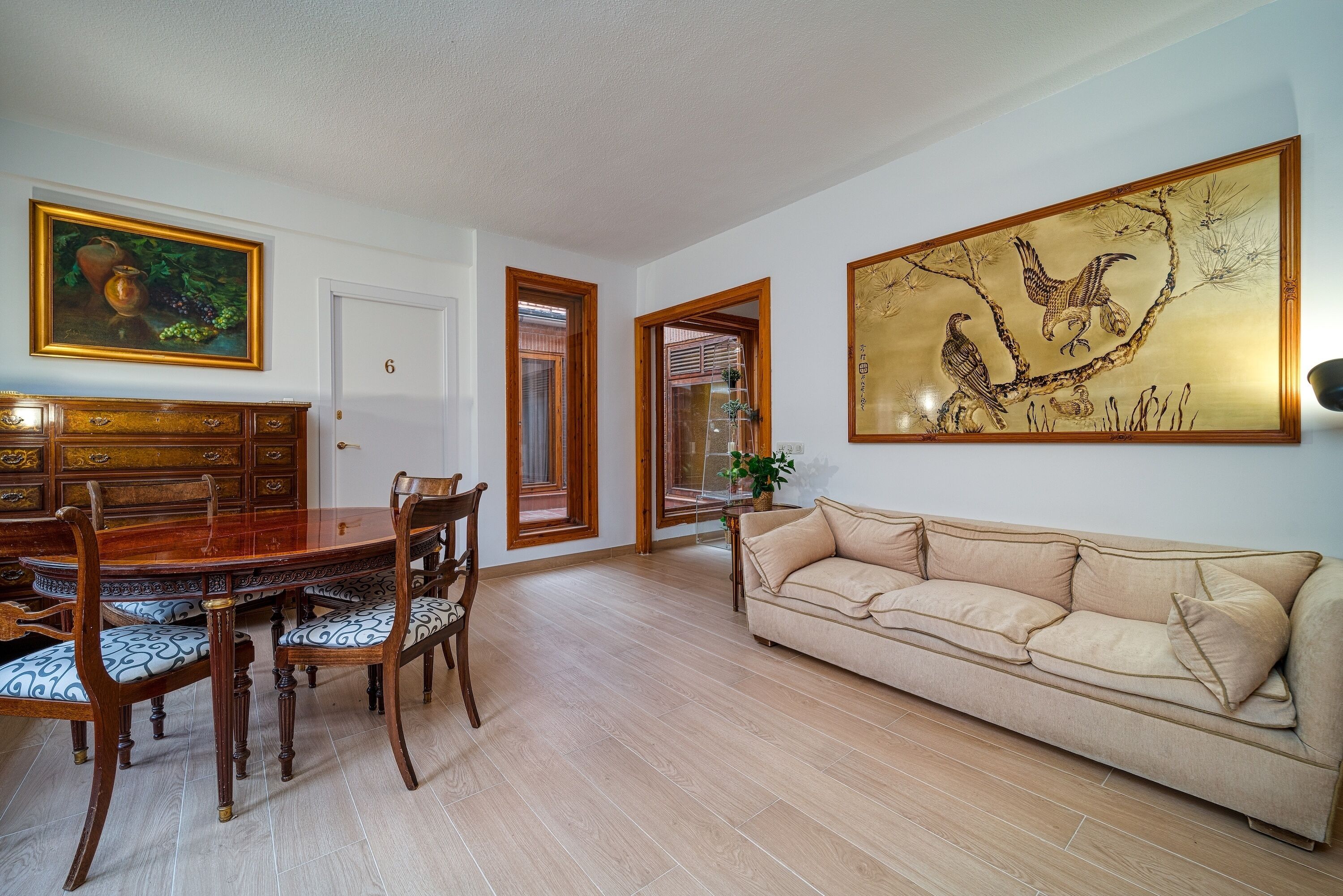 Un coin repas avec une table et des chaises en bois, un canapé beige et deux tableaux accrochés aux murs.
