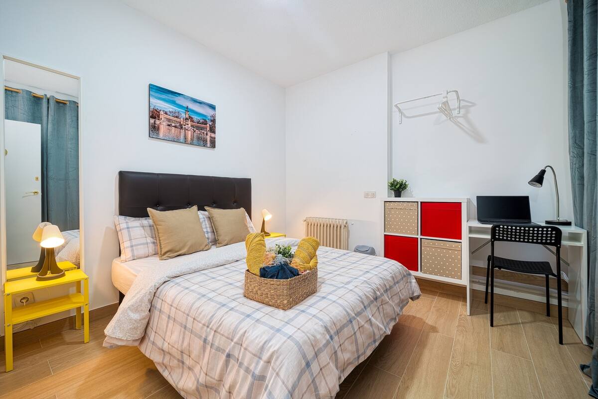 Et soveværelse med seng, sengebord, lampe og et skrivebord med stol.