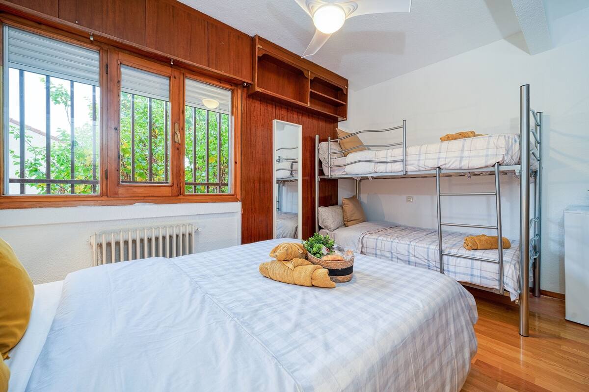 Et værelse med køjeseng, stort vindue, radiator og et natbord med en plante.