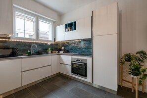 A modern kitchen with white cabinets, a built-in oven, a sink, and a window above the counter.