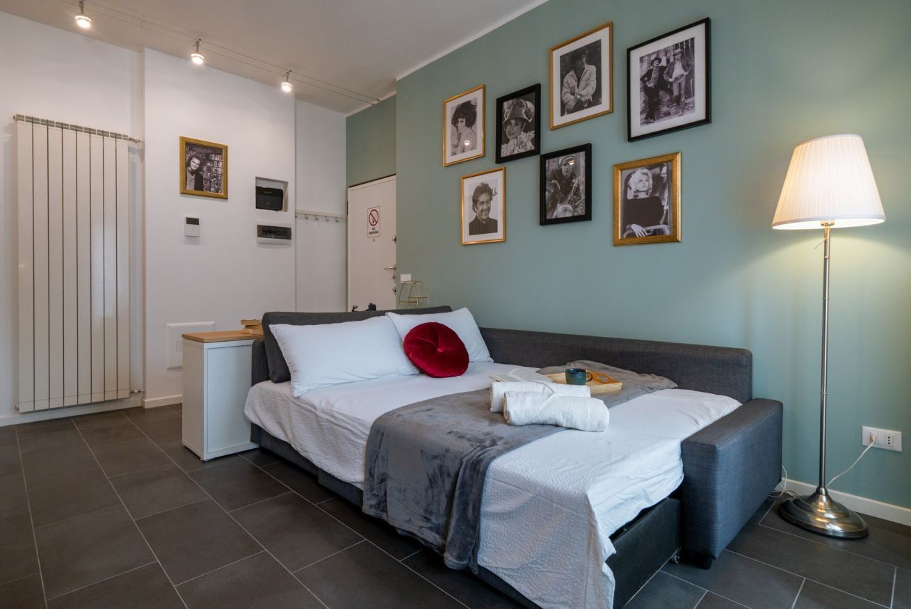 Een moderne slaapkamer met een bed, nachtkastjes, een lamp en lijstjes met afbeeldingen aan de muur.