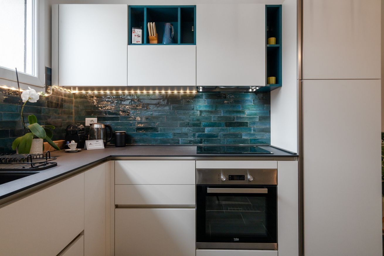 Una cocina moderna con armarios blancos, horno negro y salpicadero azul.