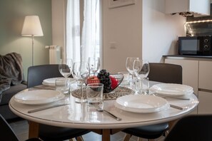 A dining table set with plates, glasses, and a fruit bowl, in a room with a sofa and a microwave in the background.