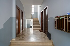 A hallway with a tiled floor, wooden doors, a staircase, and a metal locker area.