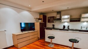 Une cuisine moderne avec un plancher en bois, un téléviseur encastré et deux tabourets de bar.