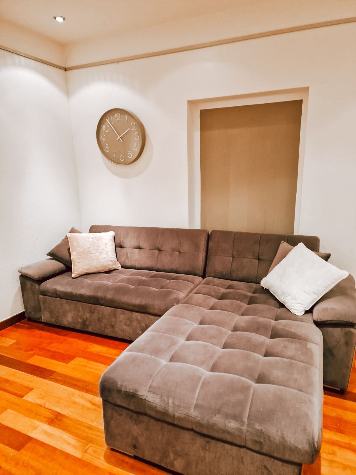 A living room with a sectional sofa, a small ottoman, and a round wall clock.
