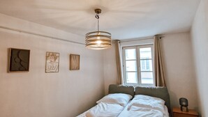 Une chambre à coucher avec un lit, une table de chevet, une lampe et une fenêtre.