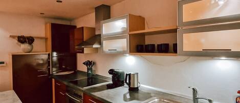 Una cocina compacta con armarios de madera oscura, un lavamanos de acero inoxidable y un horno empotrado.