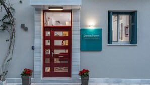 A boutique hotel entrance with a red door, a sign reading "Downtown Boutique Hotel," and two potted plants. - Downtown Hotel (Nafplio)