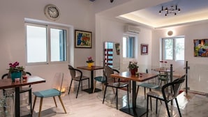 A dining area with multiple tables and chairs, a clock on the wall, and artwork. - Downtown Hotel (Nafplio)