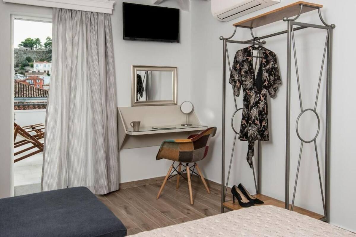 A bedroom with a bed, a desk, a chair, a hanging clothes rack, and a window with curtains.