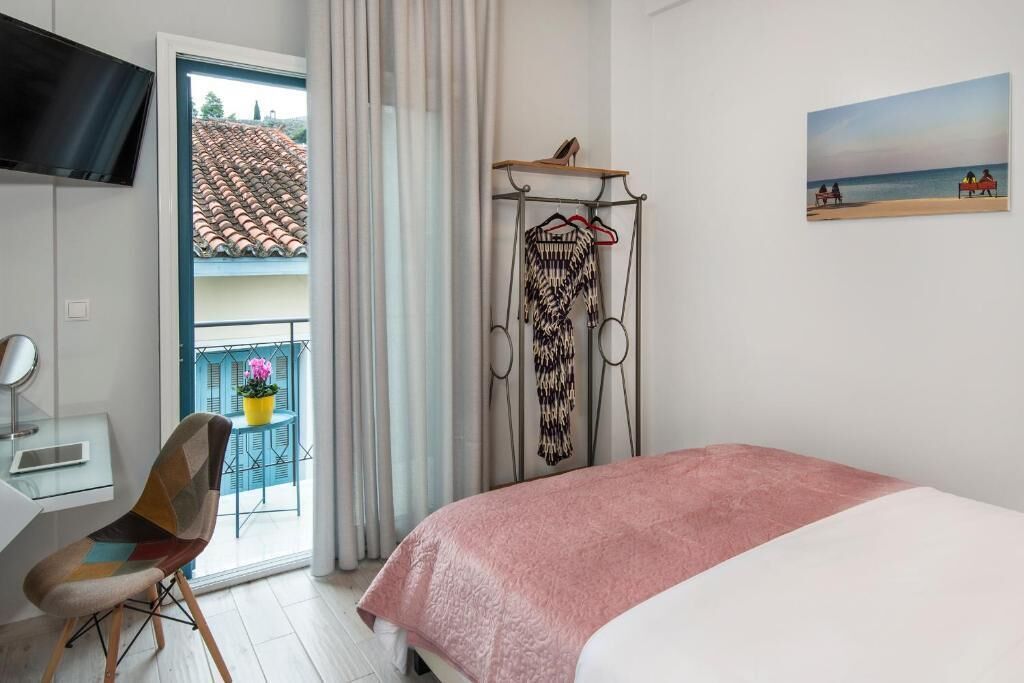 A bedroom with a bed, a chair, a TV, a balcony with a view of a tiled roof, and a painting on the wall.