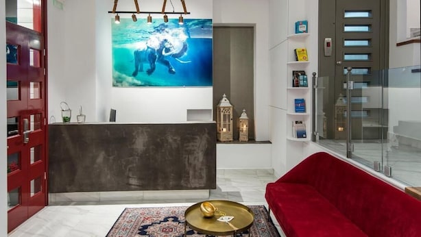 A modern living room with a red sofa, a dark reception desk, a large wall-mounted artwork, and a patterned rug. - Downtown Hotel (Nafplio)