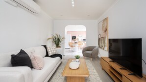 Ein modernes Wohnzimmer mit Sofa, Couchtisch, Fernseher und Blick in die Küche.