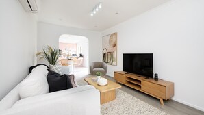 Ein modernes Wohnzimmer mit einer Couch, einem Couchtisch, einem Fernseher und einem Essbereich im Hintergrund.
