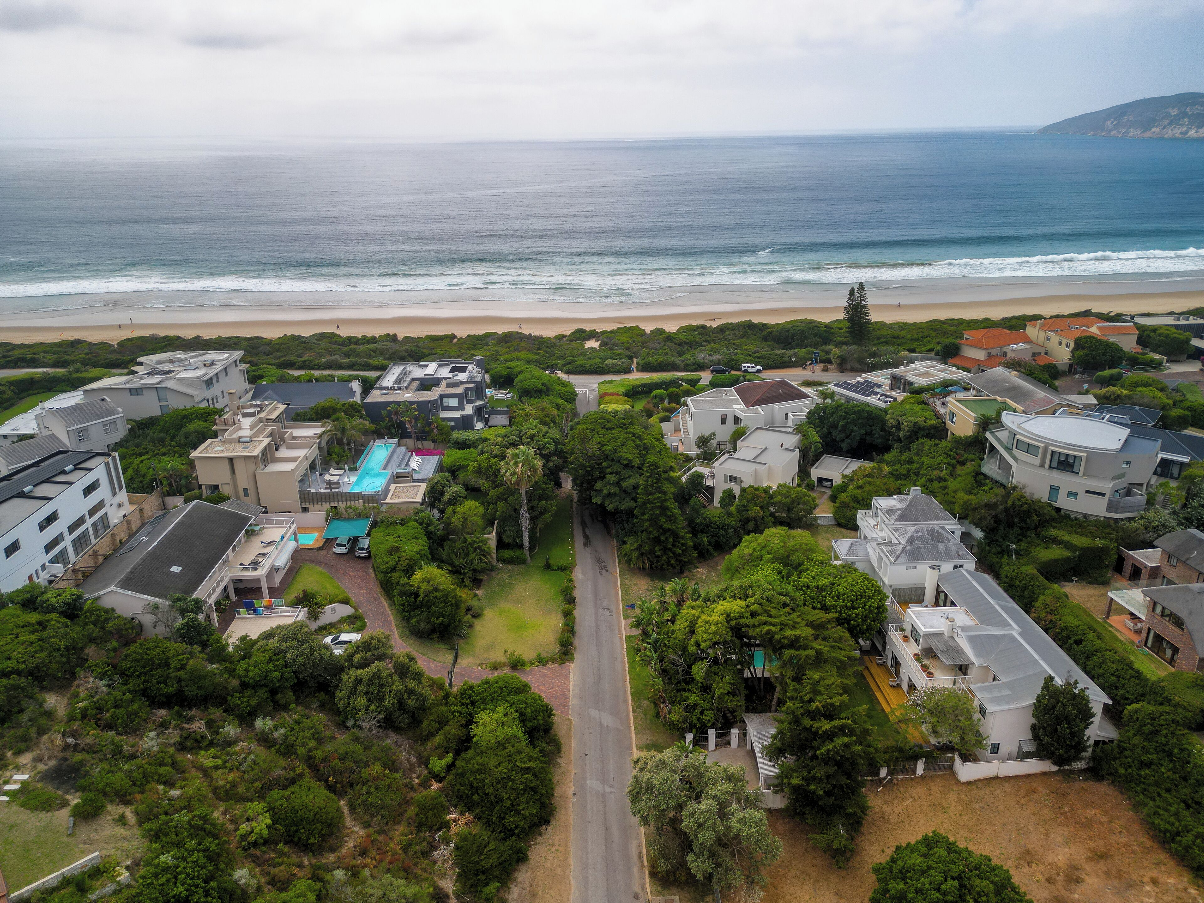 Vista aérea de una zona residencial costera con casas, piscina y una playa al fondo.