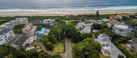 Vista aérea de una zona residencial costera con casas, piscina y una playa al fondo.
