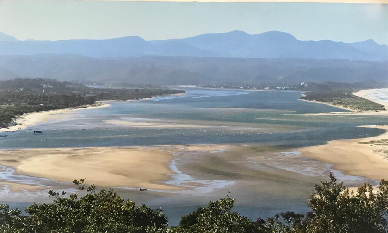 A coastal landscape with a river, beach, and distant mountains.
