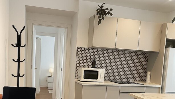 Une cuisine moderne avec des meubles blancs, un four à micro-ondes et un ordinateur portable posé sur une table.