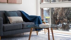 A modern living room with a grey sofa, a glass coffee table, and two abstract paintings on the wall. - Prickly Pear Stays in Merewether - Ridge St (Newcastle)