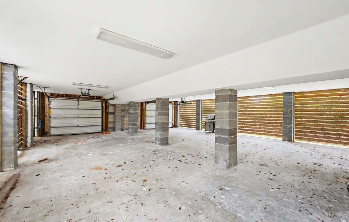 A spacious, unfinished interior with exposed concrete floors and structural columns, large garage doors, and a flat ceiling with a single light fixture.