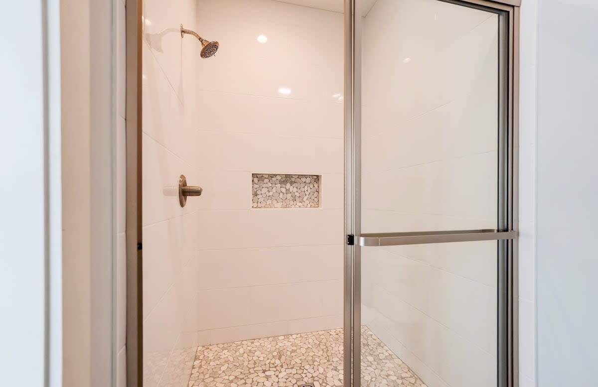 A glass-enclosed shower area with a tiled floor and a small pebble accent wall.