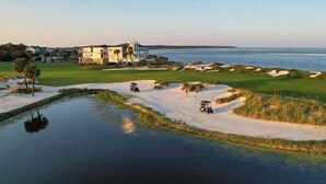 En golfbana med sandbunkrar, en vattendekoration och en stor byggnad i bakgrunden.