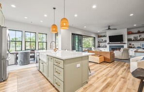 Une cuisine moderne dotée d’un grand îlot central, de luminaires suspendus et d’un téléviseur fixé au mur.