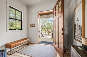 Un couloir avec un banc, une porte donnant sur l’extérieur et un tableau encadré accroché au mur.