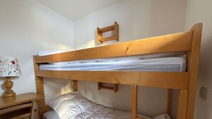 A bunk bed with a wooden frame, white bedding, and a small wooden shelf with a lamp. - Cosy apartment ski-in/ski-out (Les Allues)