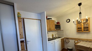 A compact kitchen with wooden cabinets, a microwave, a sink, and a dining area with a table and chairs. - Cosy apartment ski-in/ski-out (Les Allues)