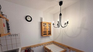 A small kitchen with a sink, wooden cabinets, a clock, a chandelier, and a table with chairs. - Cosy apartment ski-in/ski-out (Les Allues)