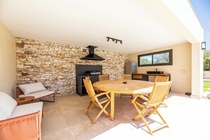 A patio area with a stone wall, a built-in grill, a round wooden table, and chairs. - Villa Anna - 10 minutes from the beach (Bonifacio)