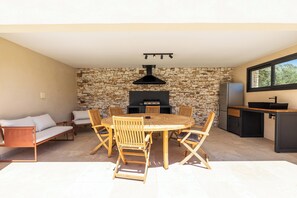Una cocina al aire libre moderna con una pared de piedra, una mesa redonda de madera y asientos.