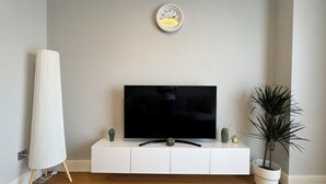 A modern living room with a flat-screen TV on a white cabinet, a tall white lamp, and a potted plant. - Stylish Taksim 360 Apartment in Central Istanbul (Beyoğlu)