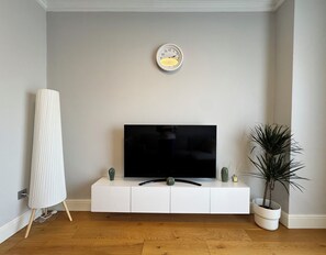 A modern living room with a flat-screen TV on a white cabinet, a tall white lamp, and a potted plant. - Stylish Taksim 360 Apartment in Central Istanbul (Beyoğlu)