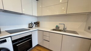 A modern kitchen with white cabinets, a built-in oven, a sink, and a kettle. - Stylish Taksim 360 Apartment in Central Istanbul (Beyoğlu)