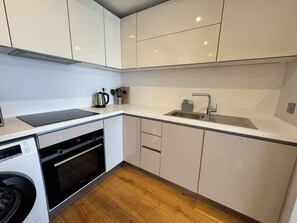 A modern kitchen with white cabinets, a built-in oven, a sink, and a kettle. - Stylish Taksim 360 Apartment in Central Istanbul (Beyoğlu)