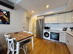 A modern kitchen with a wooden dining table, white chairs, a stainless steel refrigerator, a washing machine, and a microwave. - Stylish Taksim 360 Apartment in Central Istanbul (Beyoğlu)