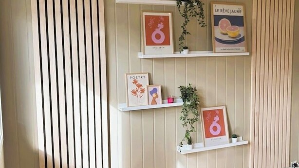 A room with wooden slat walls, a wooden floor, and shelves with framed items and plants. - Lillehammer Camping (Lillehammer)