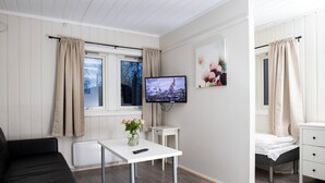 A modern room with a white sofa, a small table with a vase, a TV on the wall, and a bed with a white headboard. - Lillehammer Camping (Lillehammer)